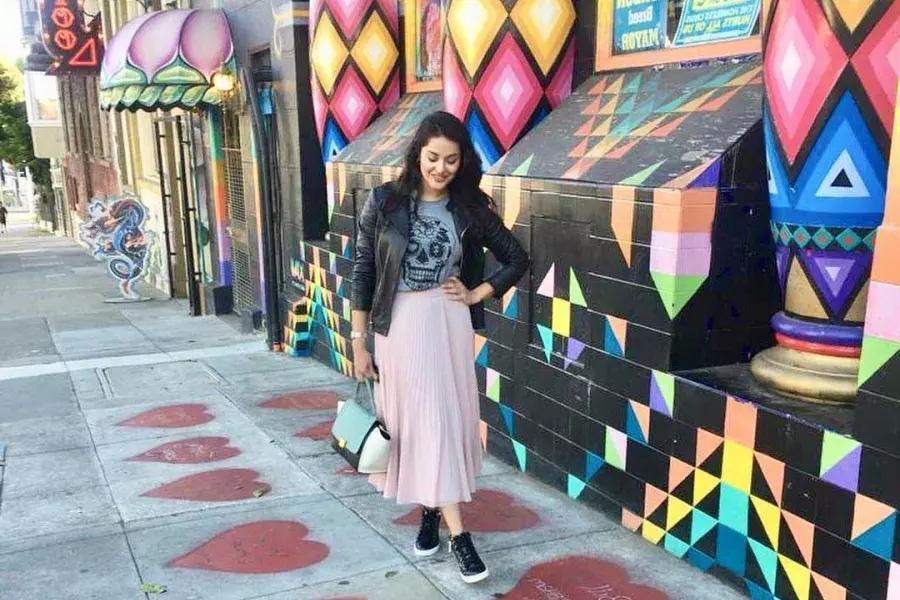 A woman stands on a sidewalk painted with red hearts, 在一个色彩斑斓的店面前, in San Francisco's 嬉皮 neighborhood.